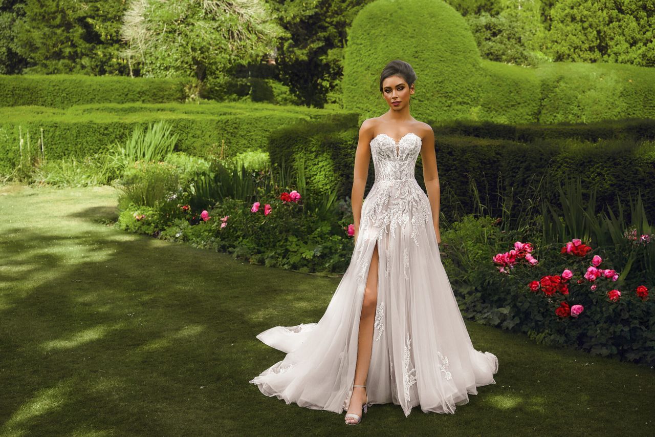 Bride in a strapless embroidered wedding gown with front slit, standing in a formal garden